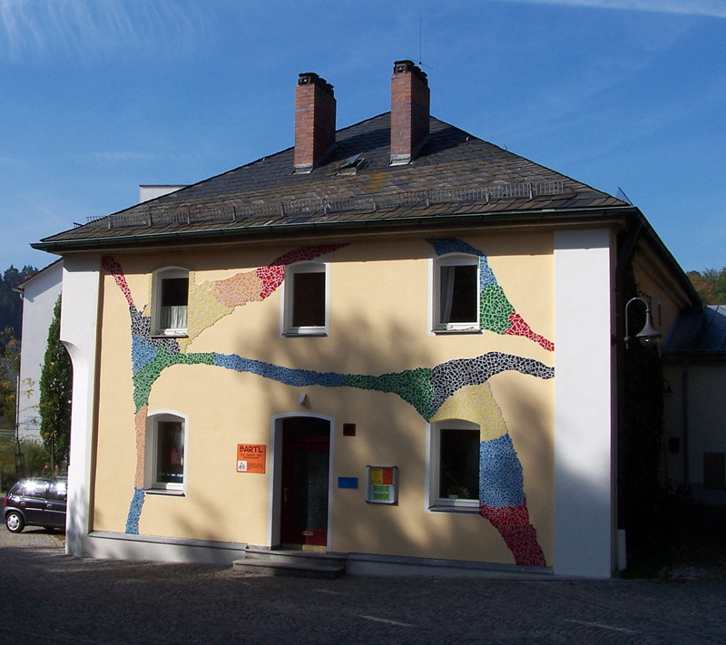 Gelbes Haus mit buntem Mosaik auf der Fassade, auf dem Türschild steht Bartl